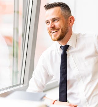 Professional businessman smiling by a window, portraying workplace positivity and confidence.