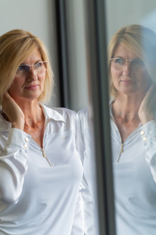 A Woman Wearing White Long Sleeve Shirt While Standing by the Glass Wall