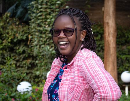 Joyful portrait of a woman laughing outdoors in Nairobi, Kenya, with sunglasses and braids.