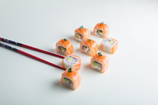 Elegant display of fresh salmon sushi rolls with chopsticks on a white surface.