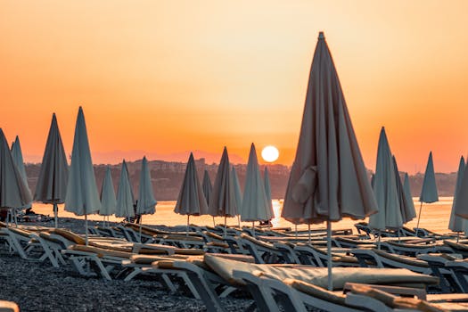 Capture the calm of a beach sunrise with sun loungers and umbrellas silhouetted against the warm sky.