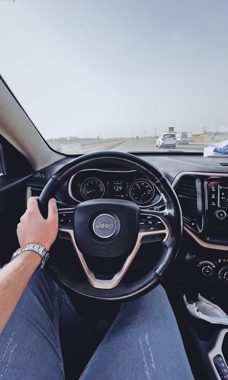 A Person In Denim Pants Controlling The Steering Wheel Of A Vehicle