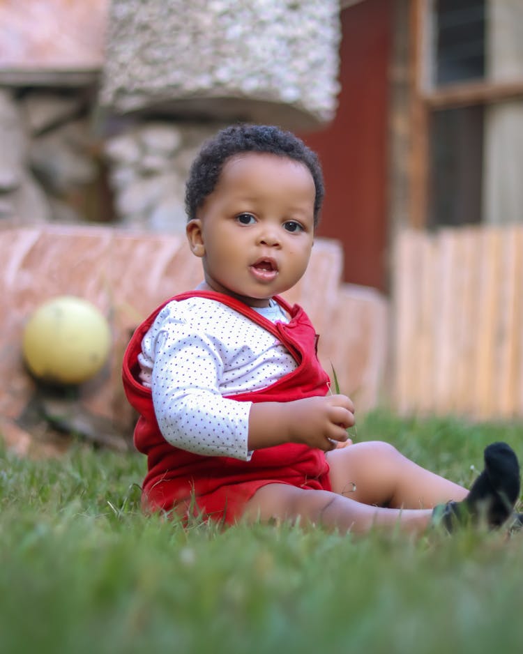 A Baby Sitting On The Grass