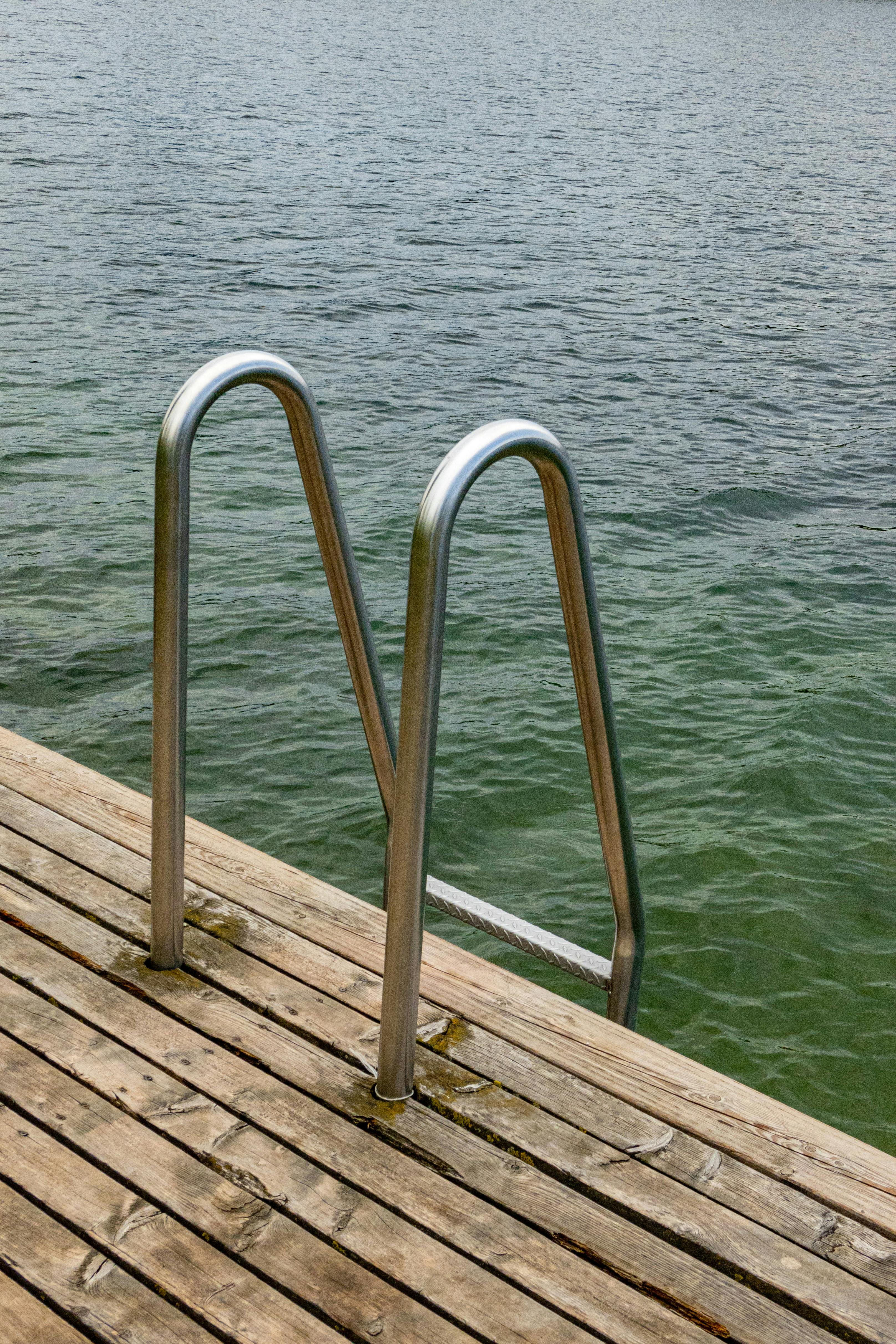 A serene view of a metal ladder on a wooden pier leading into clear blue waters. Perfect for summer relaxation.