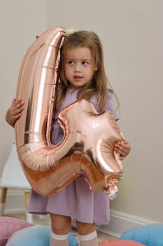 Young girl with long brown hair holding a number four foil balloon during birthday celebration.