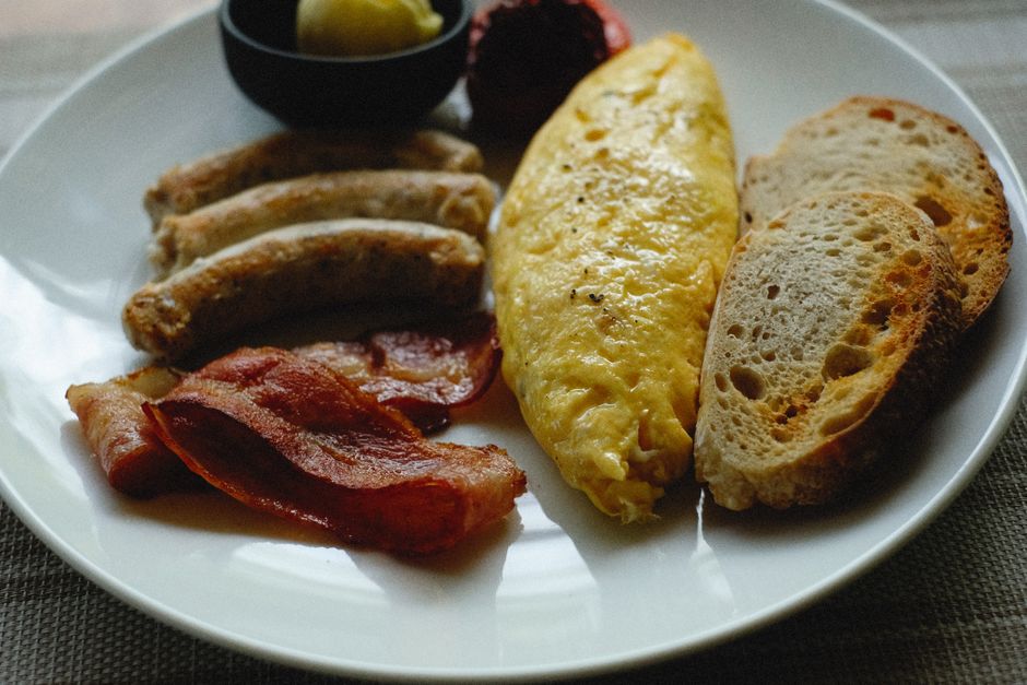 Scrumptious breakfast plate featuring omelette, bacon, sausage, toast on a ceramic plate.