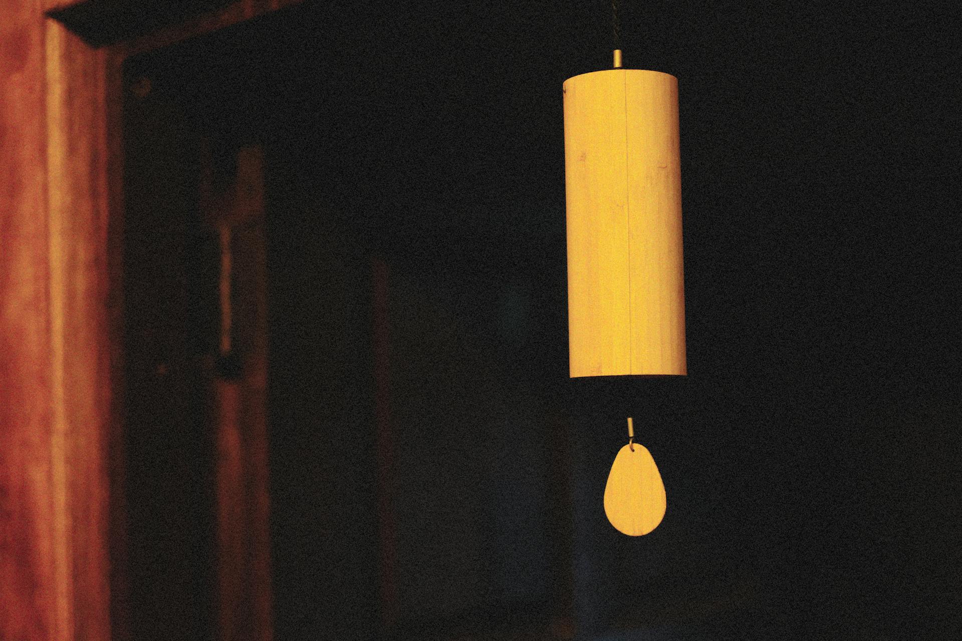 A wooden wind chime hangs in a dimly lit room, casting a warm, serene ambiance.