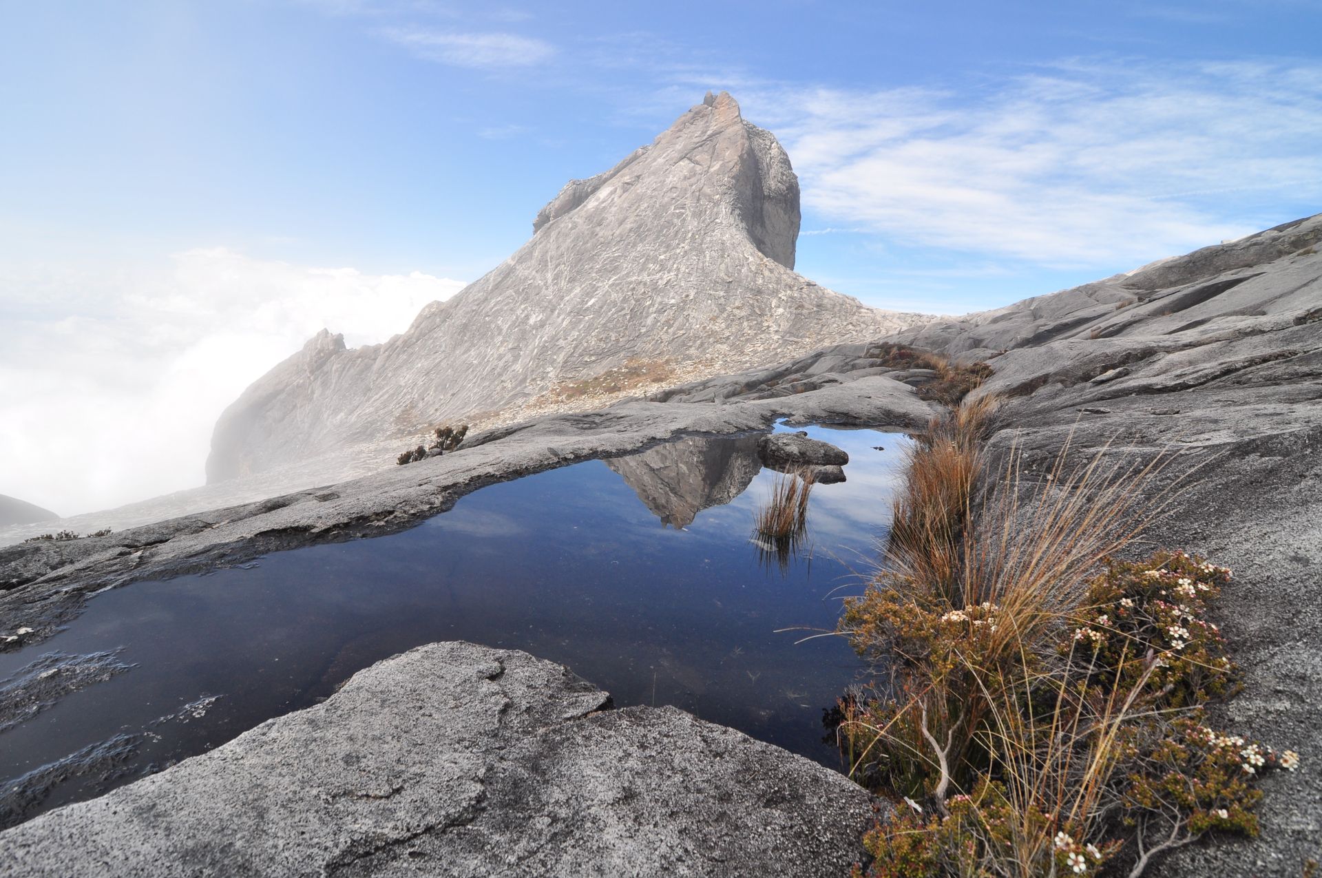 Stunning landscape of Mount Kinabalu in Sabah, Malaysia, with a reflective puddle and clear blue skies.