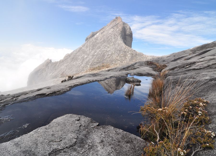 Stunning landscape of Mount Kinabalu in Sabah, Malaysia, with a reflective puddle and clear blue skies.