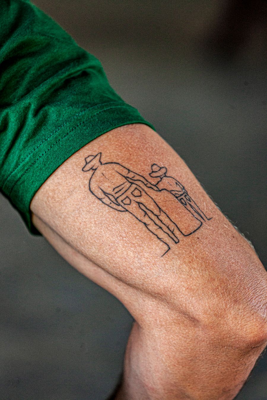 Fine-line tattoo of two figures walking on an upper arm