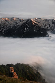 Stunning snow-capped mountain peaks rise above a cloud-filled valley, capturing serene natural beauty.