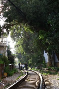 Scenic view of people walking along a railway track lined with lush green trees.