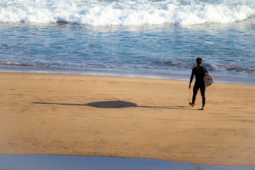 Man Carrying Surfboard While Walking on Shore