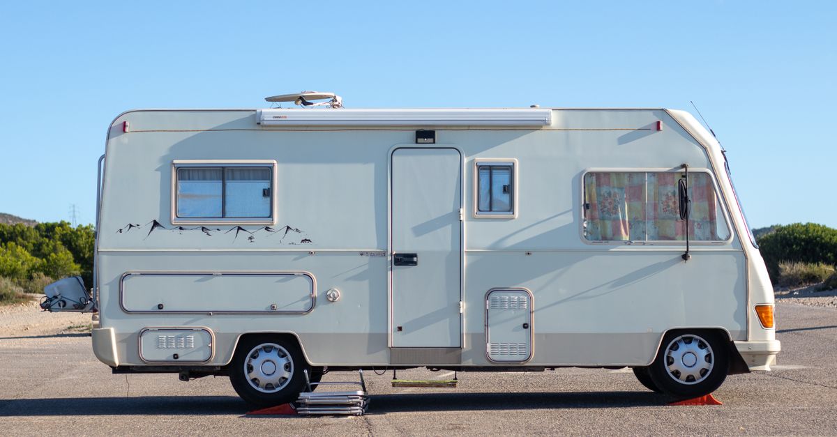 Side view of a vintage camper van parked on an open road under clear blue skies.