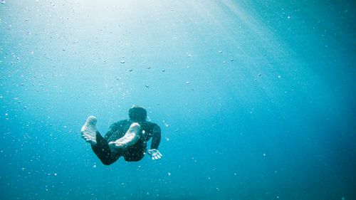 Free A captivating shot of a lone diver gracefully swimming underwater, surrounded by sunlight. Stock Photo