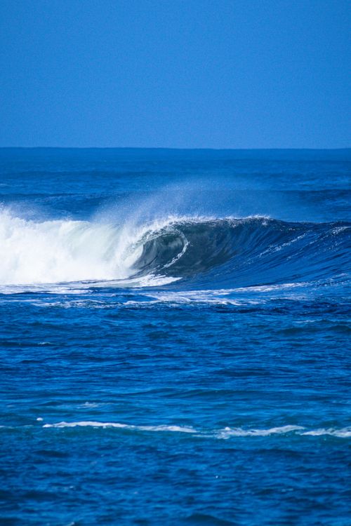 Free A stunning vertical shot of a crashing ocean wave under a vibrant blue sky. Stock Photo