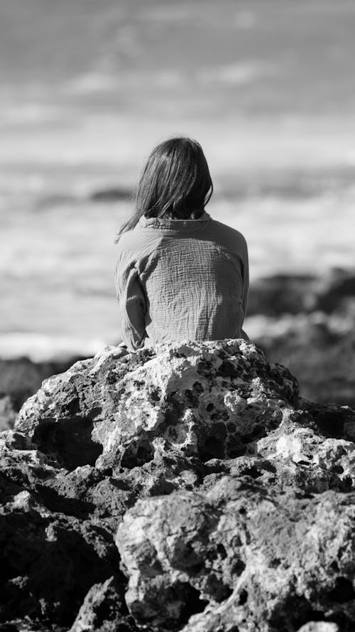Grayscale Photo of a Person Sitting on the Rock