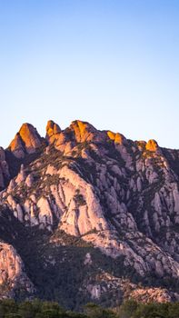 A breathtaking view of rocky mountain peaks under a clear blue sky at sunset, showcasing nature's beauty.