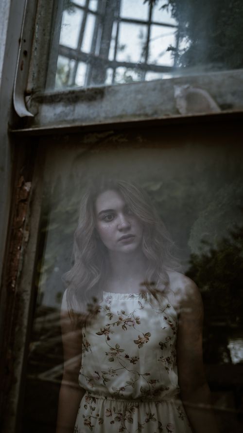 Free Reflective portrait of a woman in floral dress seen through rustic window with soft natural light. Stock Photo