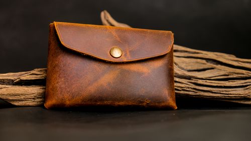 Free Close-up of a brown leather coin purse resting on rustic wood with a dark background. Stock Photo
