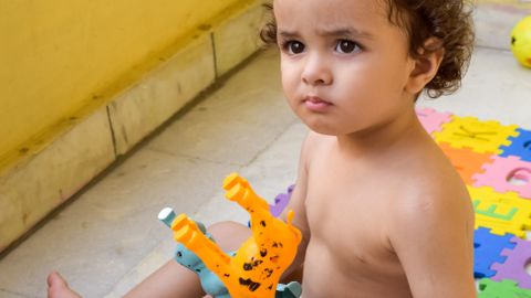Cute toddler focused on playing with colorful plastic toys indoors on a sunny day.