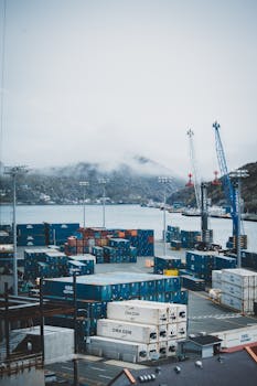 A foggy port scene with stacked cargo containers and cranes, showcasing logistics and freight operations.