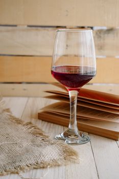 A glass of red wine sits next to an open book on a rustic wooden table.
