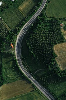 High angle aerial view of a winding road through lush green farmland and forests.