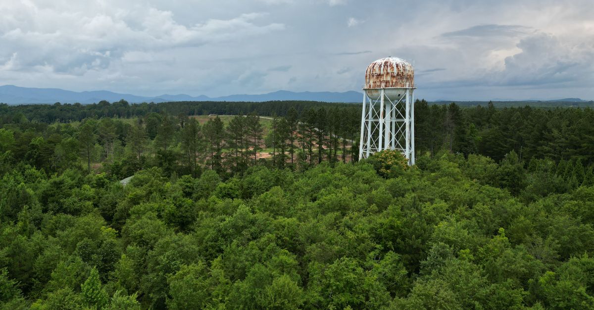 Aerial view of a rusty water tower surrounded by lush green forest in Campobello, South Carolina.