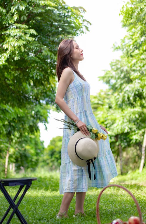 Free Woman in Blue Dress Holding Flowers and a Hat Stock Photo