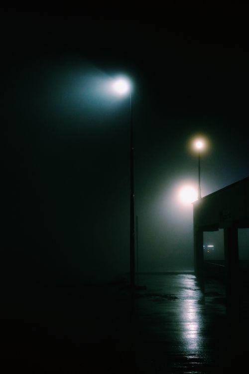 Free A misty urban street at night illuminated by lampposts, creating a dramatic atmosphere. Stock Photo