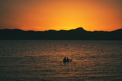 Free People swimming at sunset with a serene mountain backdrop, capturing nature's beauty. Stock Photo