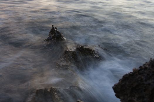 Long exposure capturing ocean waves crashing over coastal rocks at twilight.