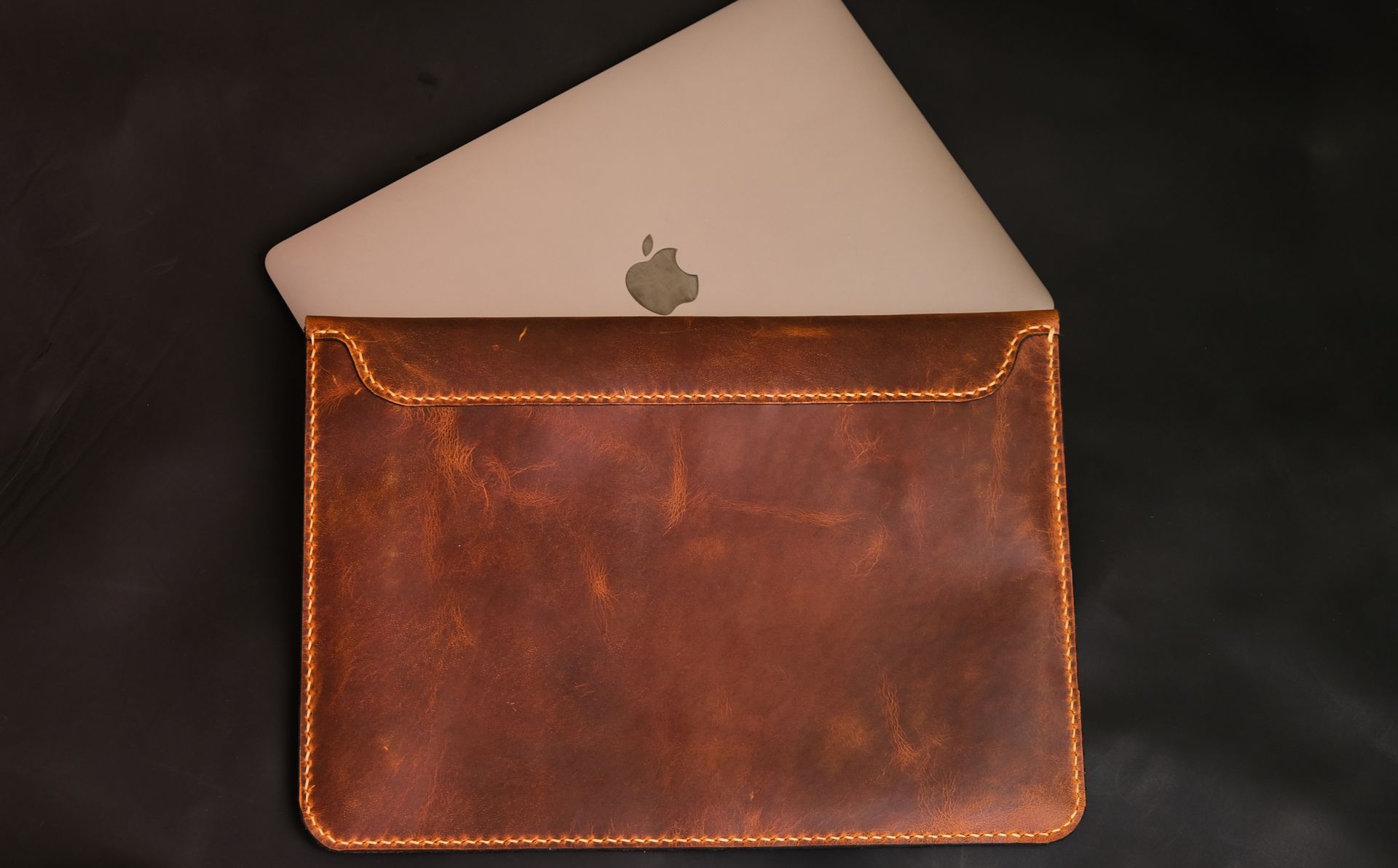 Close-up of a laptop in a stylish brown leather case against a dark background.