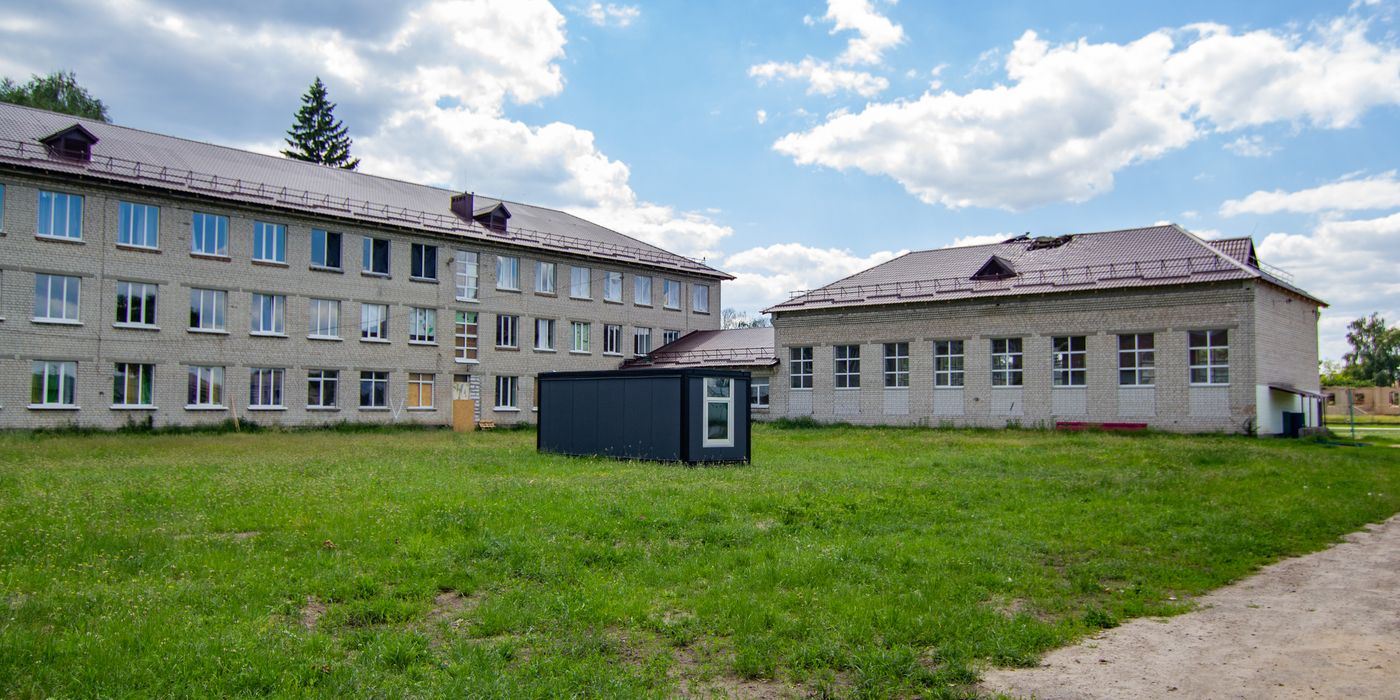 A three-story school structure surrounded by greenery and a clear sky.