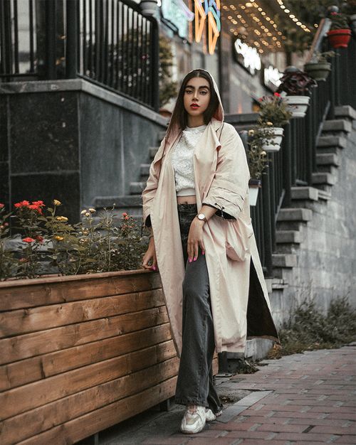 Free Fashionable woman in long coat posing near flowers and stairs in city. Stock Photo