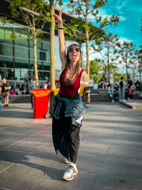 Free Energetic woman posing joyfully outside a modern building in bright sunlight. Stock Photo
