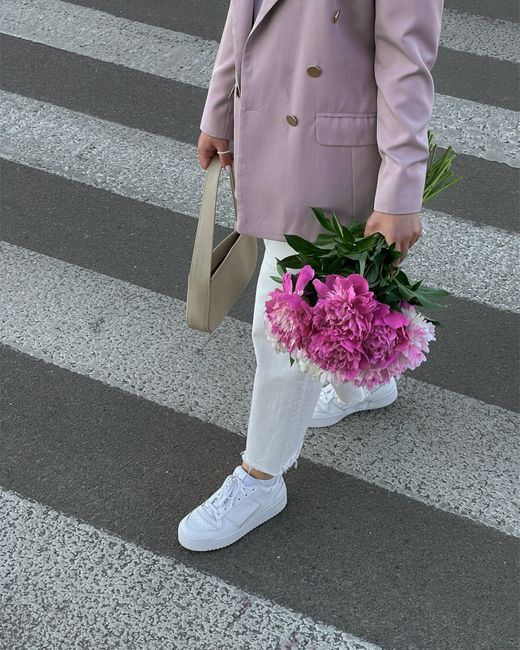 Stylish woman in pink blazer crossing street with peonies in Kyiv. Trendy urban fashion.