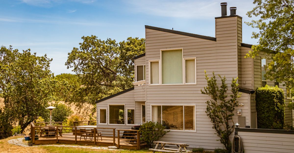 Contemporary suburban house featuring large glass windows and a spacious deck in a lush outdoor setting.