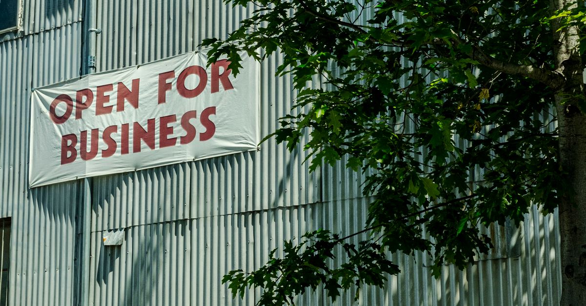 Photo by David McElwee Industrial building facade with 'Open for Business' sign shaded by tree branches.
