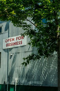 Photo by David McElwee Industrial building facade with 'Open for Business' sign shaded by tree branches.