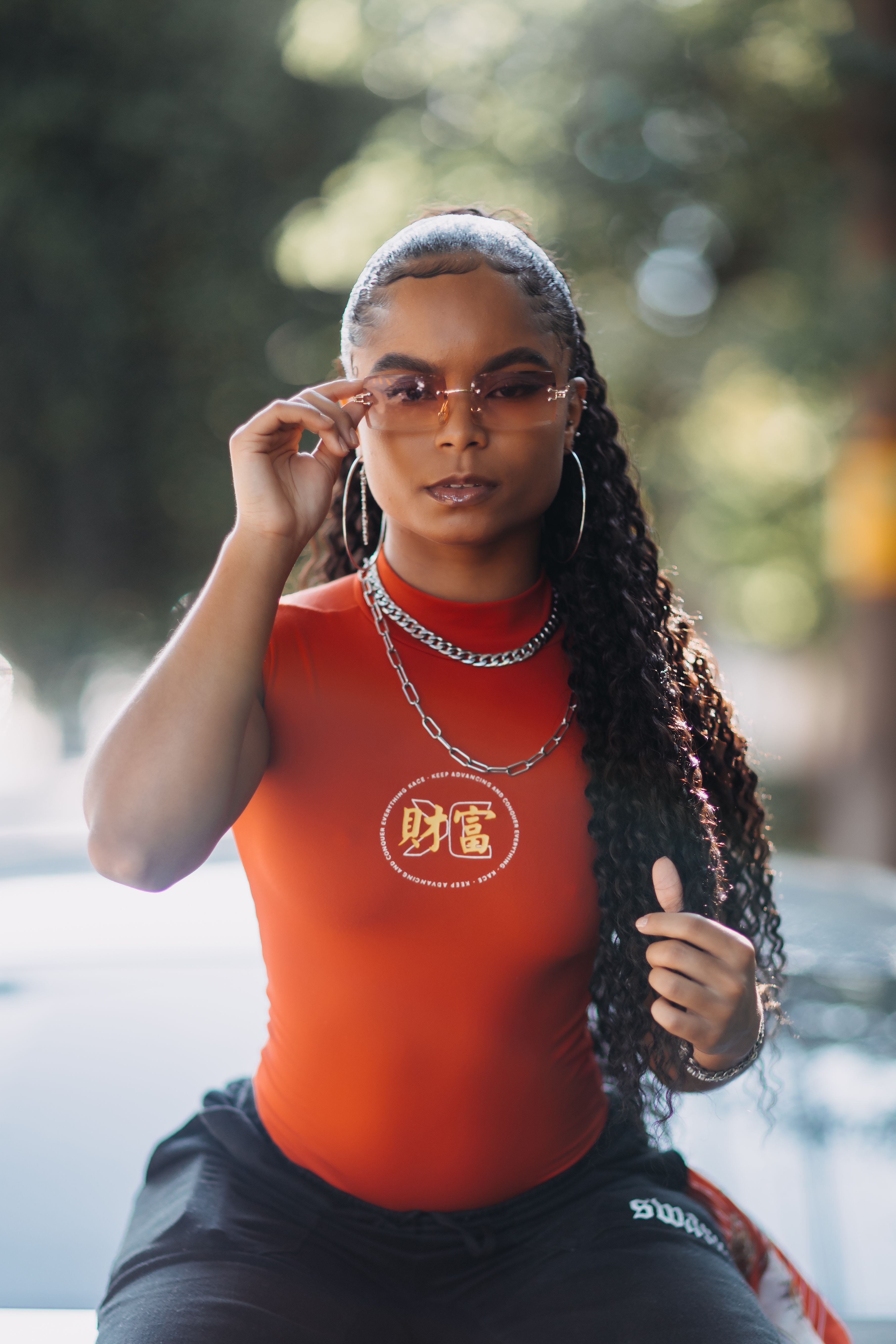 Woman with long hair and sunglasses striking a pose outdoors in vibrant attire.
