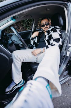 Fashionable man posing in car with sunglasses, exuding confidence and style.