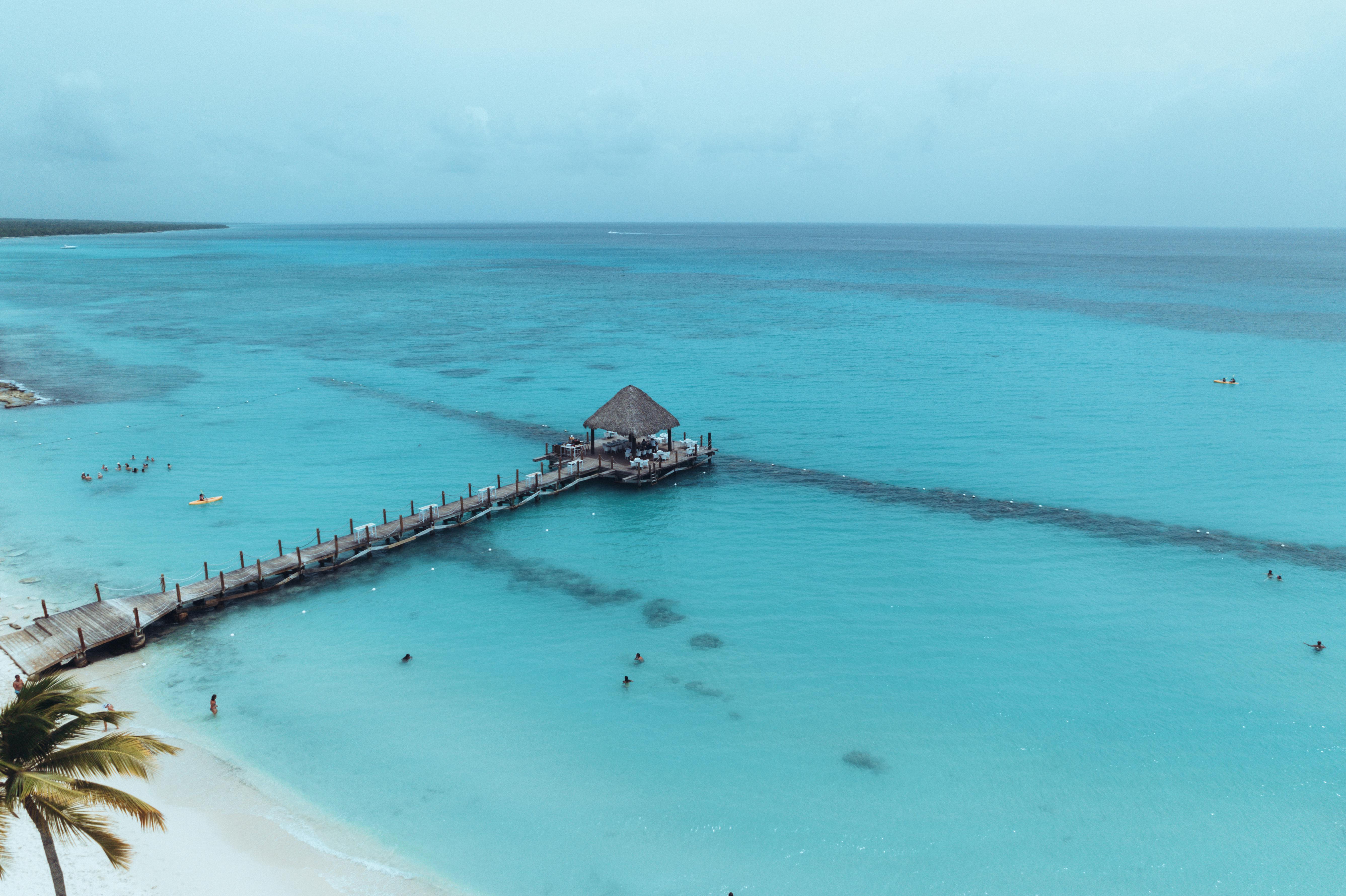 Aerial view of a tranquil tropical beach with a wooden pier extending into the vivid turquoise sea.