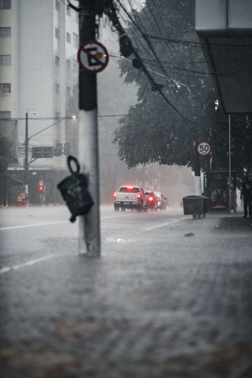 Free Moody urban street scene during heavy rainfall, featuring cars and illuminated street signs. Stock Photo