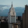 A tall, historic financial skyscraper in downtown São Paulo standing against a moody, overcast sky at dusk.