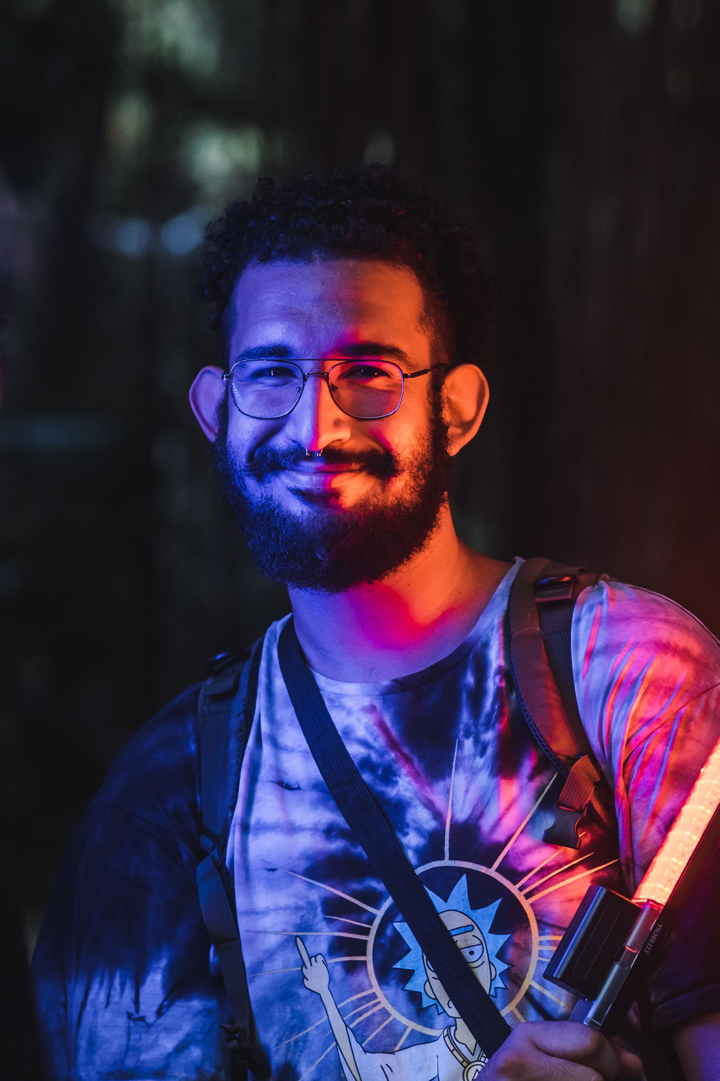 Portrait of a smiling man with neon lights in a dark, mysterious forest setting.