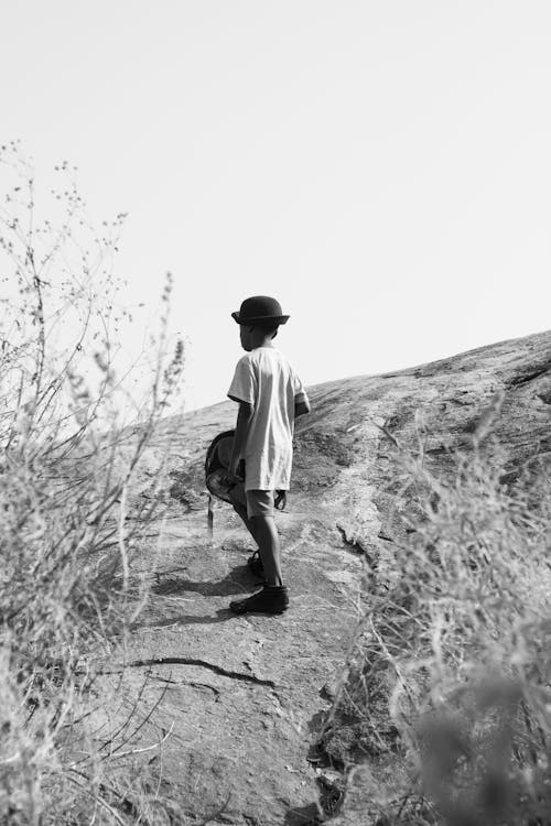 Grayscale Photo of a Boy Standing on the Hill