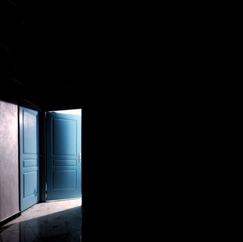 A mystical blue door partially open, casting light and shadows on a dark Moroccan interior.