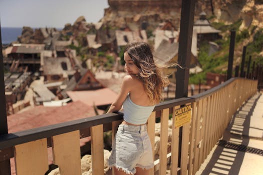 Woman in casual summer outfit admiring the view at an outdoor attraction with rustic houses.